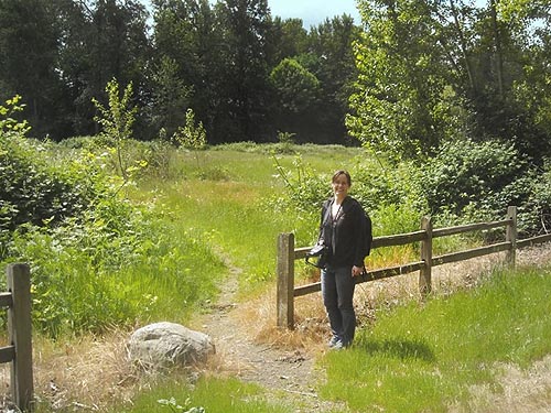 Lynette Schimming at entrance to large grassy field, Puyallup Riverwalk Trail, Pierce County, Washington