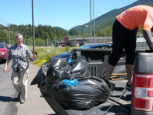 Laurel and Natalie manhandle giant bags of litter and moss, gate area of Green River Watershed, King County, Washington